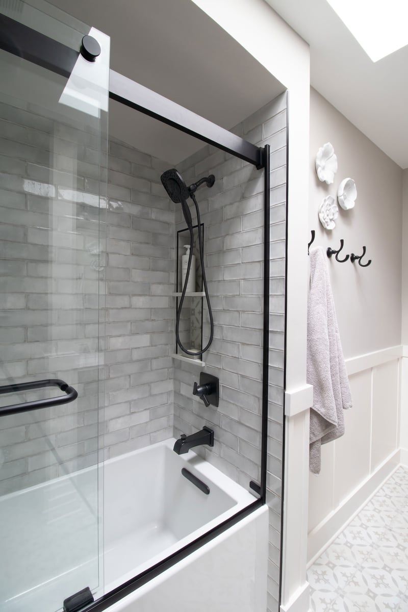 Hackney Pearl 3x9 tile (field) with Decora Redondo (niche), Kohler Underscore Tub, Kohler Levity Shower Doors, Delta Ashlyn Series Matte Black fixtures