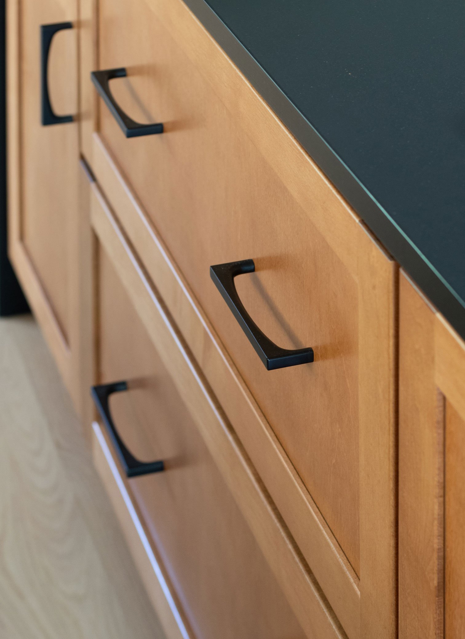 Warm wood stained cabinets with black quartz countertop and black hardware detail