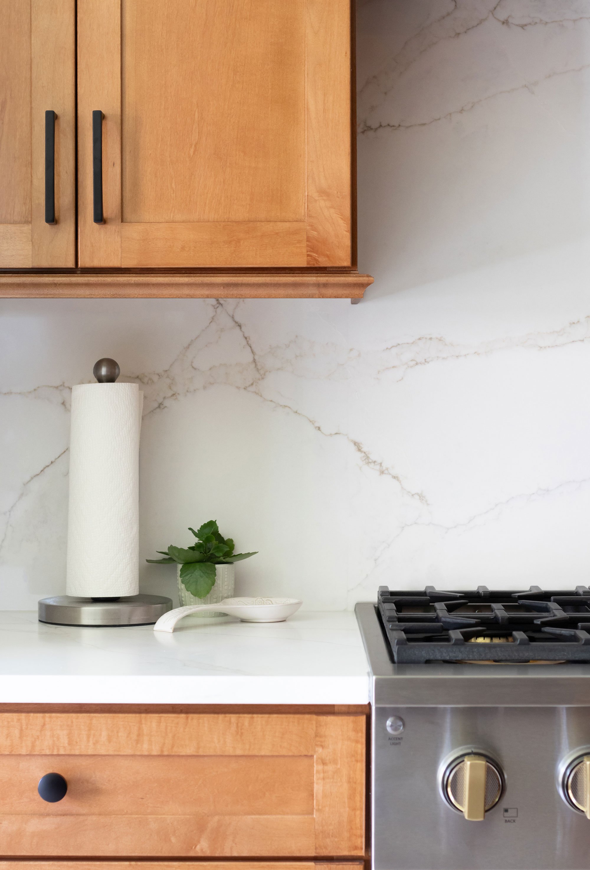 Warm wood stained cabinetry, white quartz countertop and backsplash, and range detail